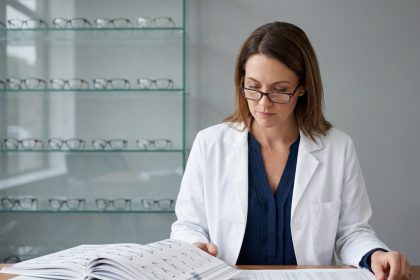 Opticienne analysant des catalogues fournisseurs et des marges commerciales dans l'arrière-boutique d'un magasin d'optique